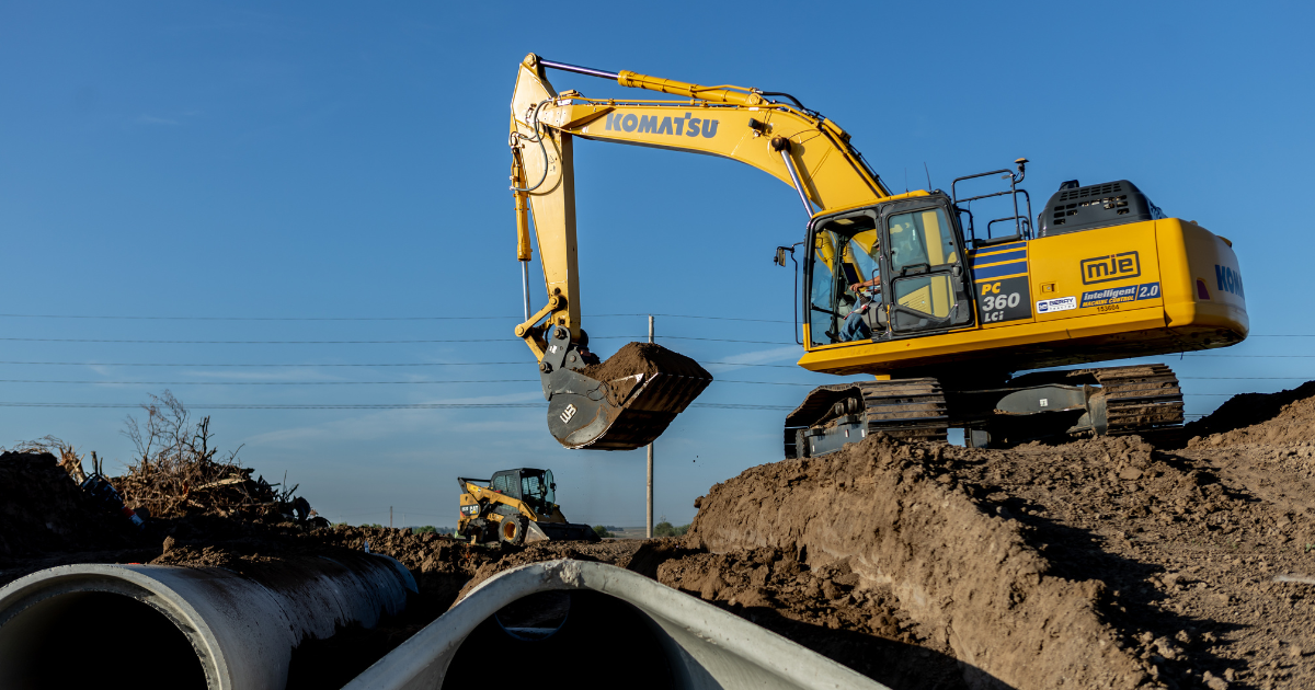 A large excavator adds dirt to highway concrete culvert. 
